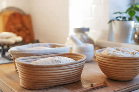 Preparations of sourdough Bread in rasstoechnye rattan baskets are on the table. The girl makes incisions with a knife and puts it in the oven to bake. The interior of a home kitchen. Homemade sourdough bread with your own hands.の写真素材