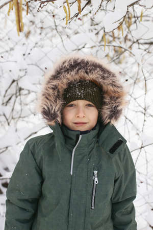 Portrait of a boy dressed in warm clothes, in winter in snowy weather on the street.