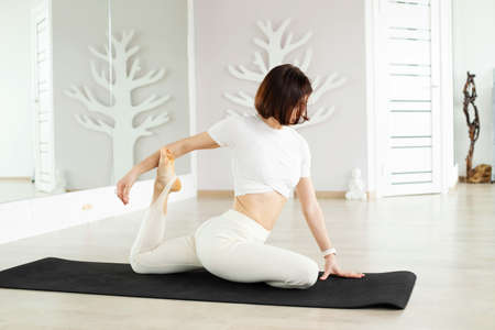 A young brunette girl does yoga, meditates on the floor in the studio, hall.の写真素材