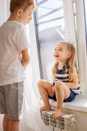 Kids brother and sister playing hide and seek behind the curtain girl laughing and having fun.の写真素材