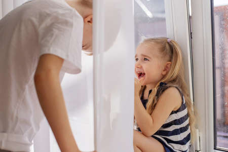 Kids brother and sister playing hide and seek behind the curtain girl laughing and having fun.の写真素材