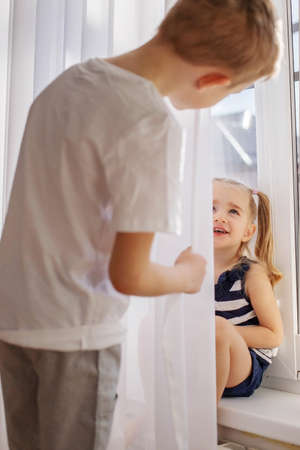 Kids brother and sister playing hide and seek behind the curtain girl laughing and having fun.の写真素材
