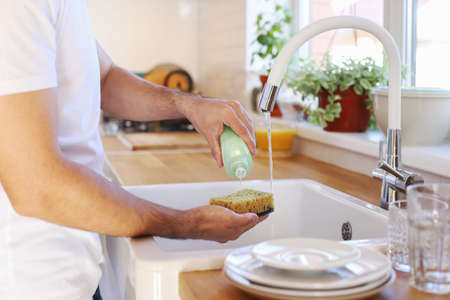 A man washes dishes, eco-friendly dishwashing detergent, a sponge for washing dishes made of eco-friendly materials.の写真素材