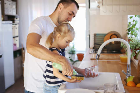 Dad and daughter are washing dishes in the kitchen. Family life, house cleaning.の写真素材