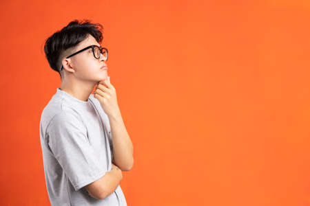 Portrait of young asian man with cryptic expression, isolated on orange backgroundの写真素材