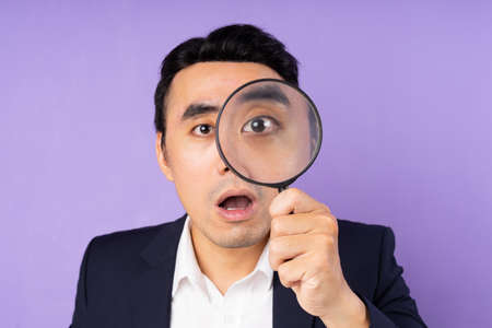 Business man in suit wearing magnifying glass, isolated on purple backgroundの写真素材
