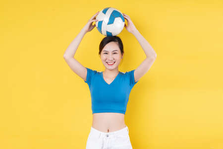 portrait of young dynamic girl holding ball in hand isolated on yellow backgroundの写真素材