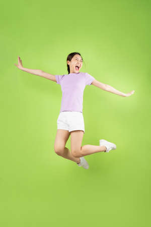 Full body Young Asian girl jumping, isolated on green backgroundの写真素材