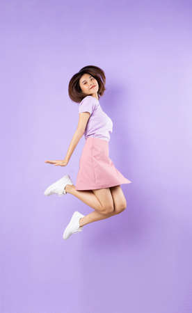 Young asian girl jumping up on purple backgroundの写真素材