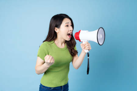 portrait of young asian girl, holding phone, isolated on blue backgroundの写真素材