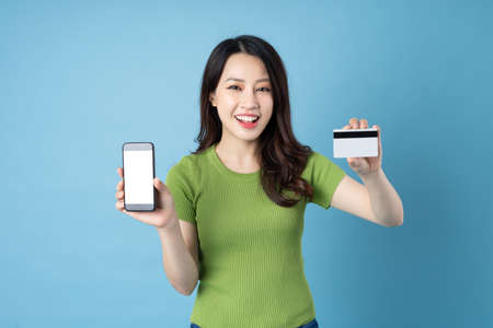 portrait of young asian girl, holding phone, isolated on blue background