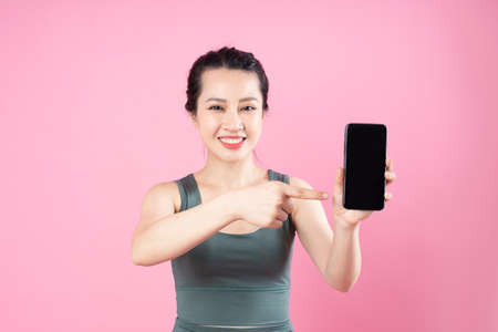 portrait of young asian girl, holding phone, isolated on blue backgroundの写真素材