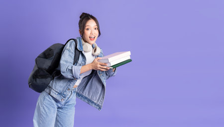 Portrait of a beautiful Asian schoolgirl wearing a backpack on a purple background