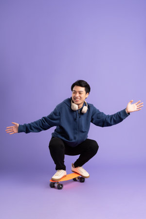 Image of young Asian man playing skateboard on purple backgroundの写真素材