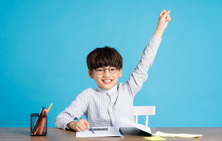portrait of school boy sitting and studying on a blue backgroundの写真素材