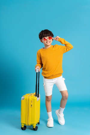 Asian boy pulling suitcase on blue backgroundの写真素材