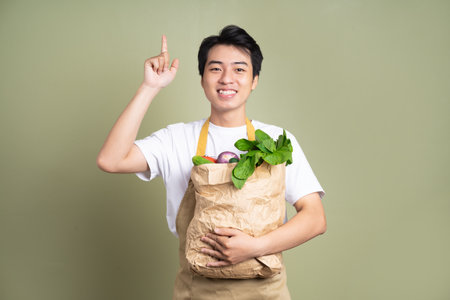 Young man is holding a bag full of vegetables, on white background.の写真素材