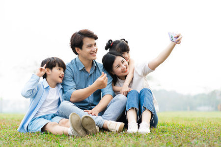 image of an asian family sitting together on the grass at the parkの写真素材