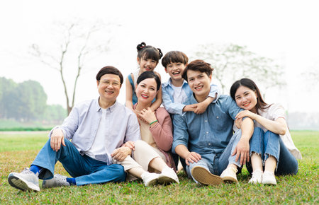 image of an asian family sitting together on the grass at the parkの写真素材