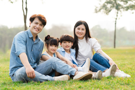 image of an asian family sitting together on the grass at the parkの写真素材