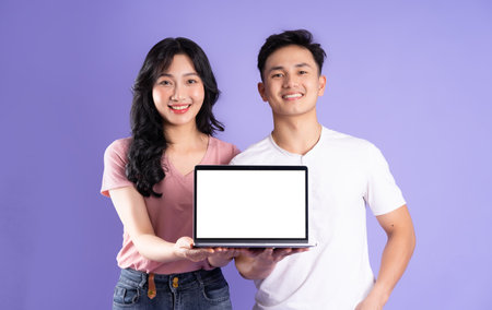 image of asian couple using laptop, isolated on purple backgroundの写真素材