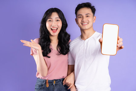 image of asian couple holding smartphone, isolated on purple backgroundの写真素材