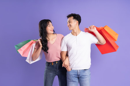 image of asian couple holding shopping bags on purple backgroundの写真素材