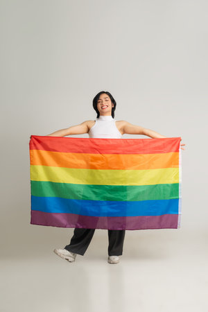 Image of Asian gay man holding a rainbow flag confidently posing on a white backgroundの写真素材