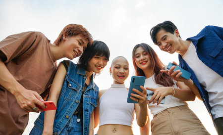 Image of a group of young Asian people laughing together and using their phonesの写真素材