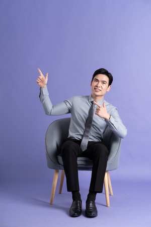 Portrait of Asian business man sitting on sofa, isolated on purple backgroundの写真素材