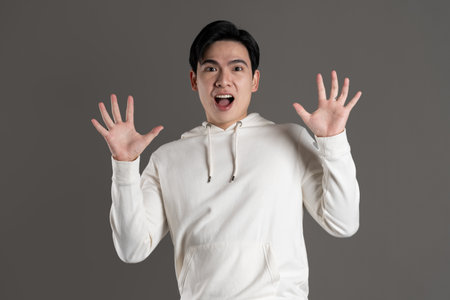 Portrait of Asian man wearing hoodie and posing on gray background