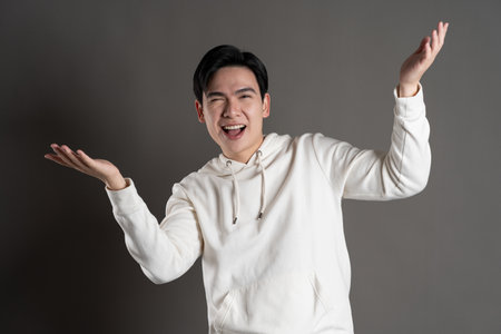 Portrait of Asian man wearing hoodie and posing on gray background