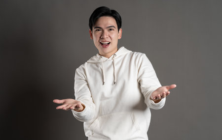 Portrait of Asian man wearing hoodie and posing on gray background