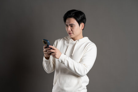 Portrait of Asian man wearing hoodie and posing on gray background