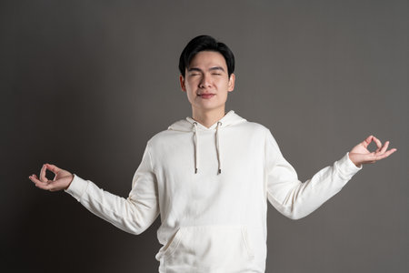 Portrait of Asian man wearing hoodie and posing on gray background