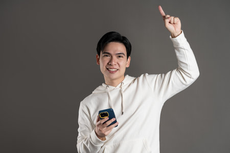 Portrait of Asian man wearing hoodie and posing on gray backgroundの写真素材