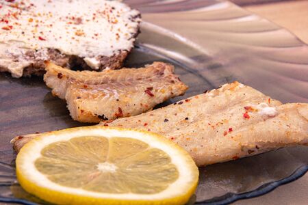 Close up of fried sea fish with spices, lemon and bread on the table