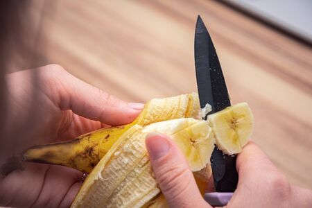 Sharp black knife cutting slices of a ripe sweet bananaの写真素材