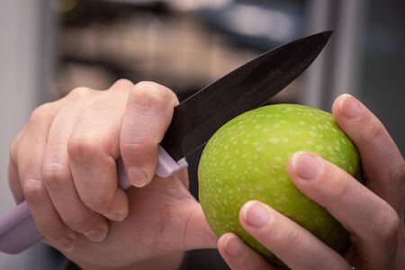 Cutting a big round green apple with a black knifeの写真素材