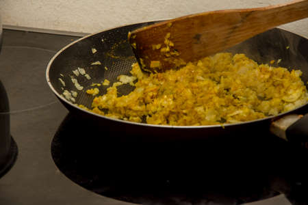 Mixing and frying onion with Indian orange and yellow condiments in the black panの写真素材