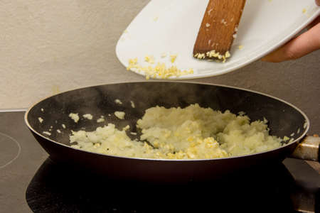 Putting garlic on the fried golden onion in the black hot panの写真素材