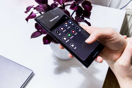 Vienna / Austria / November 14, 2020: Woman holding the black smartphone in her hand over the violet...
