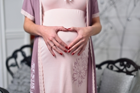 Pregnant girl holding hands on stomach in heart shapeの写真素材