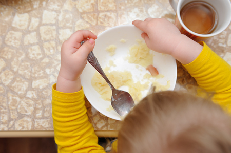 A little girl eats her dinner at the tableの写真素材