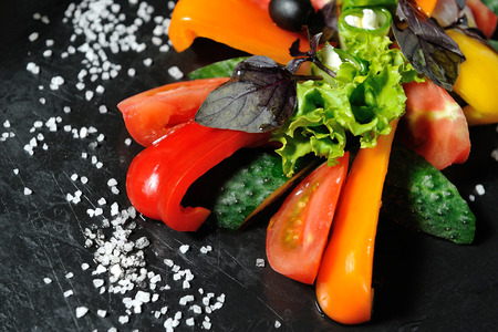 Sliced vegetables on a wooden board in a restaurant, cucumbers, tomatoes, peppers, lettuce leaves.の写真素材