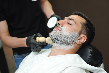 Hairdresser applies a foam brush on his face to shave his beard.の写真素材
