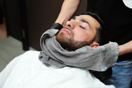 Barber preparing man face for shaving with hot towel on face in barber shop.の写真素材