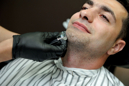 A man in a male barber shop shaves his beard with a trimmer.の写真素材