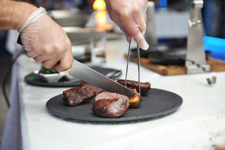 Chef, cuts pieces of meat cooked on fire to put it nicely on a plate, cooking show.の写真素材