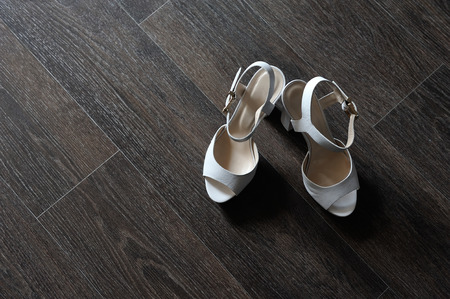 Women's beautiful shoes in white leather. White shoes stand on the dark floor of the laminate.の写真素材